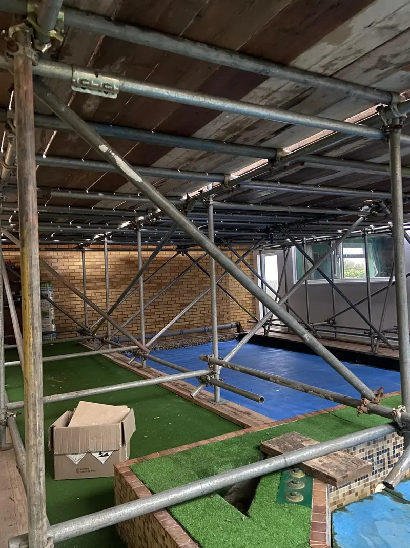 Crash-deck roof scaffold in a tight rear garden, sheeted on the inside to keep dust off the astroturf