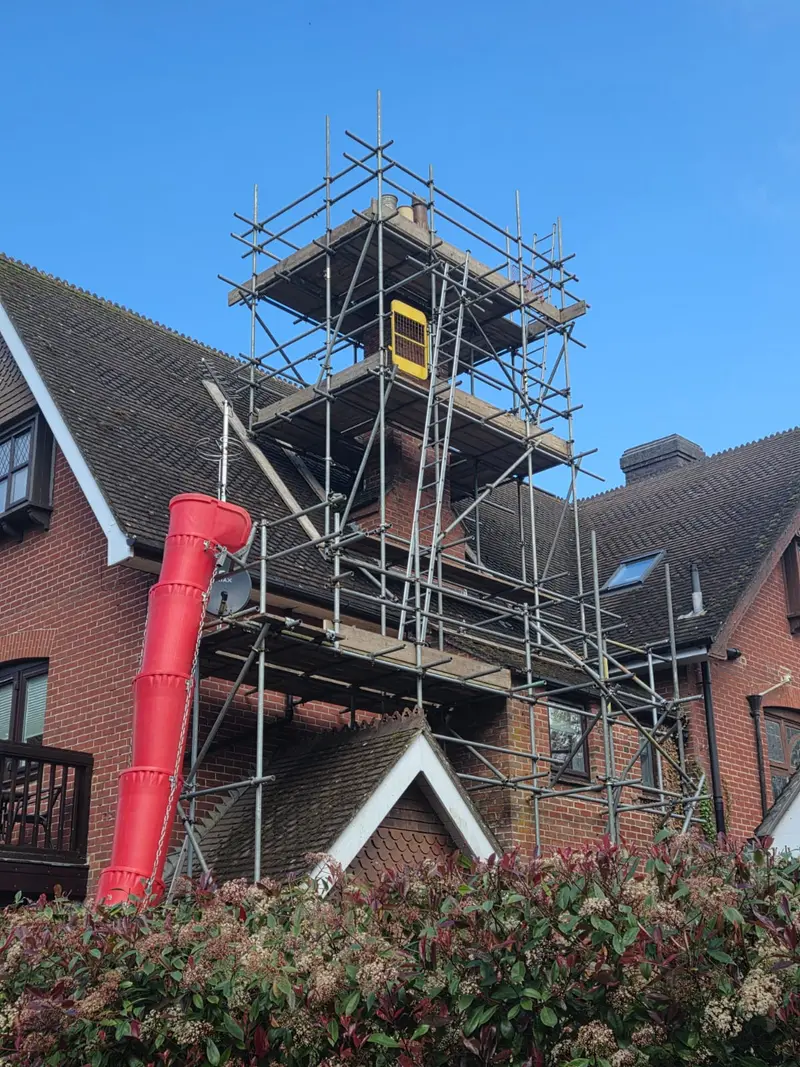 Chimney-access tower rising above the roof line of a detached house, with a red rubbish chute running down the gable